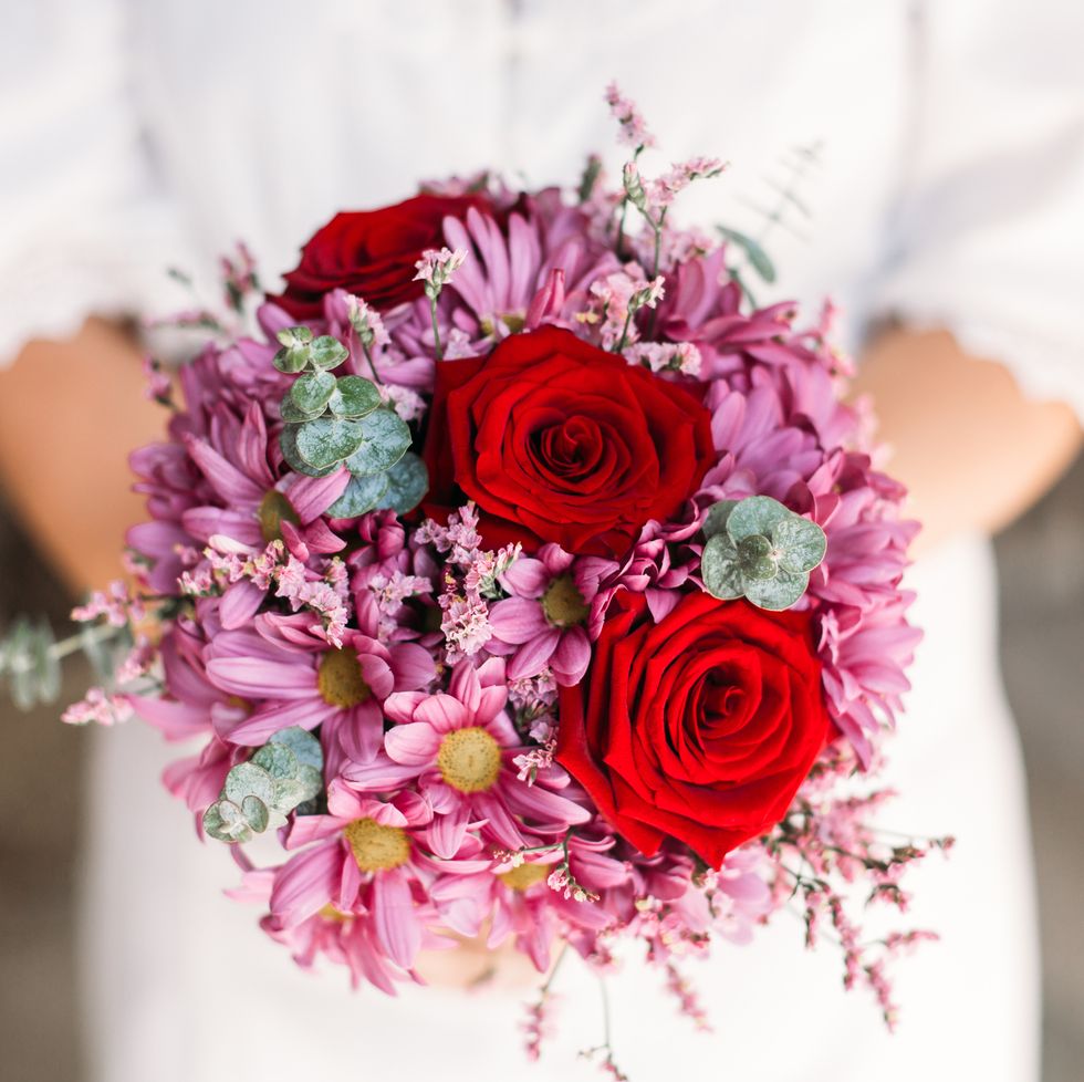 red roses and pink flowers in a bridal bouquet being held by an unidentified bride in white