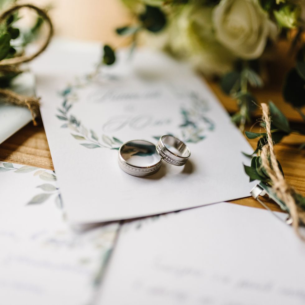 stylish wedding rings and flowers set on top of wedding invitations on wooden table