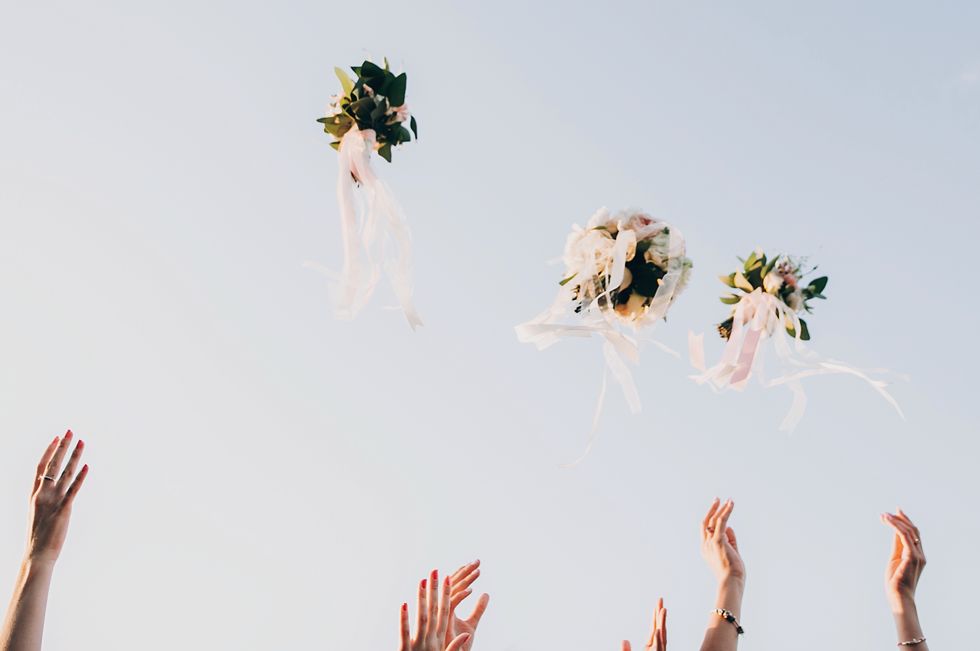 bride and bridesmaids throwing wedding bouquets up in the sky in evening soft light stylish wedding bouquets with ribbons in sky happy moment