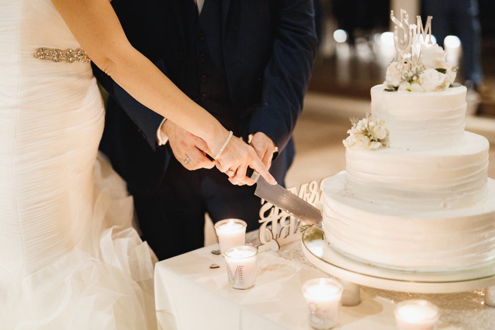 bride and groom cutting three tiered cake in white frosting together at a wedding party, close up