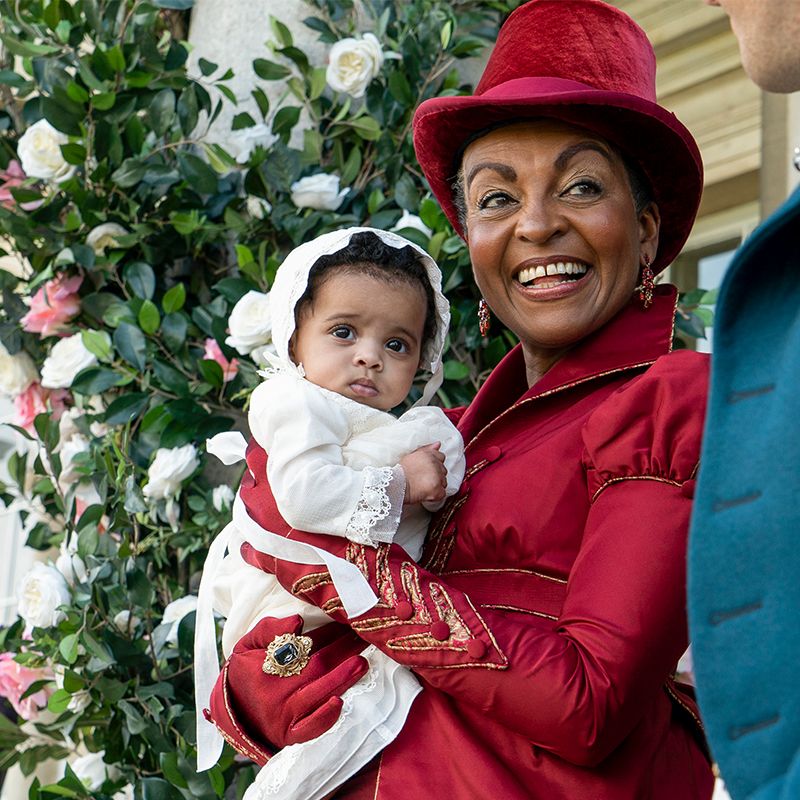 lady danbury dressed in red holding baby augie in season 2 bridgerton