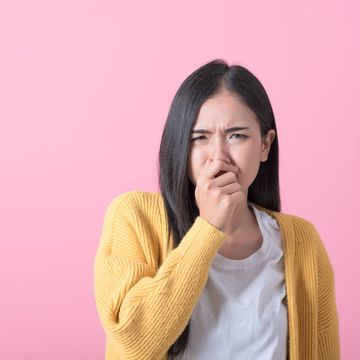 bright young woman covers his nose due to bad smell isolated on pink background