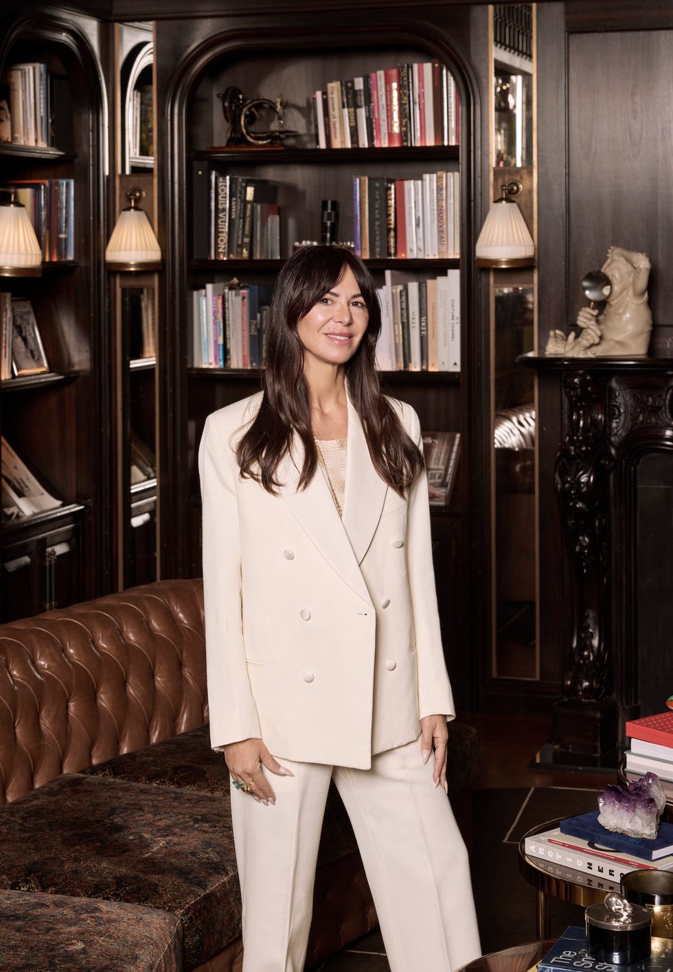 a stylish individual in a white ensemble stands in an elegant room filled with books and decor