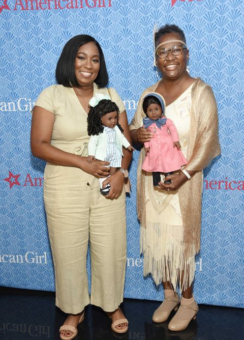 brit bennett holds the claudie doll and connie porter holds the addy doll in front of an american girl step and repeat
