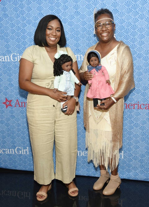 brit bennett holds the claudie doll and connie porter holds the addy doll in front of an american girl step and repeat