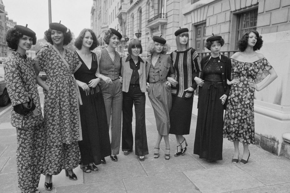mary quant stands in the middle of eight models on a sidewalk who are wearing clothes she designed