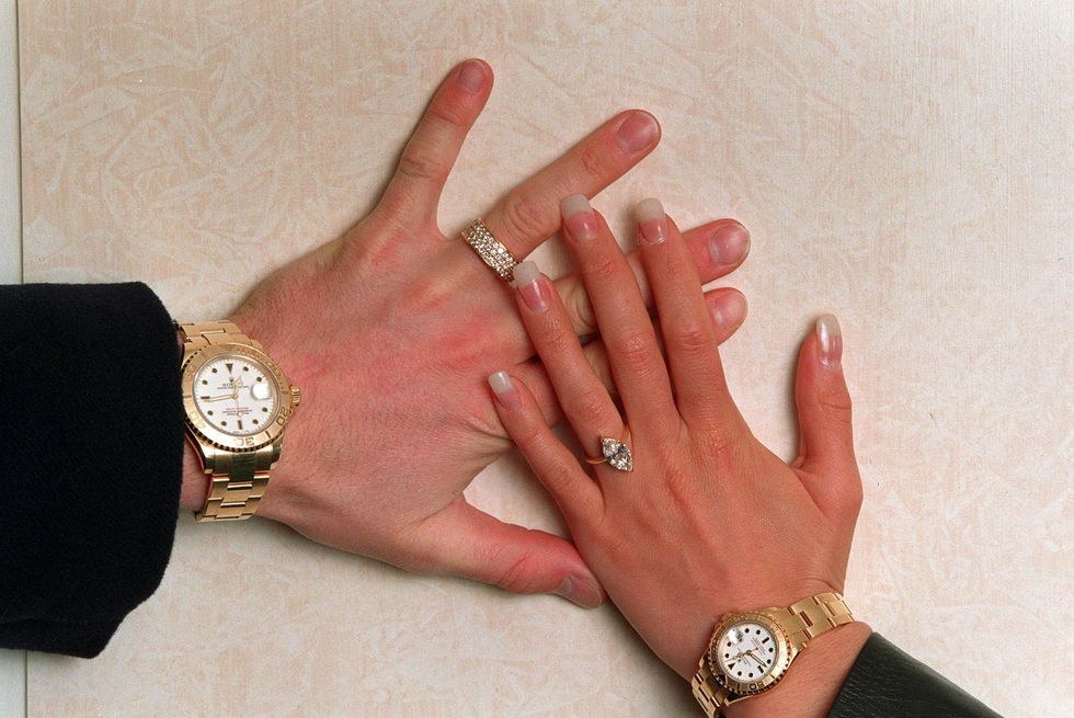 david beckham and victoria adams rest their left hands on a wall, each wears a gold watch and a ring on their ring finger