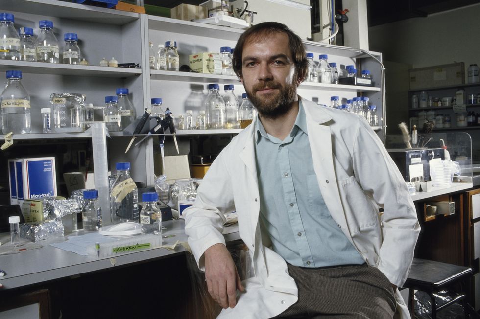 man in a lab coat sitting in front of shelves with science equipment