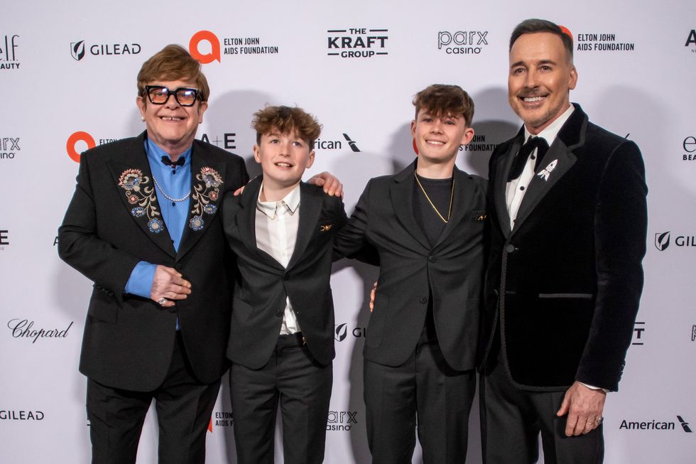elton john stands with two boys and his husband as all four people smile for photos