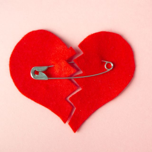 a broken heart sewn with safety pins against pink background heartbreak concept