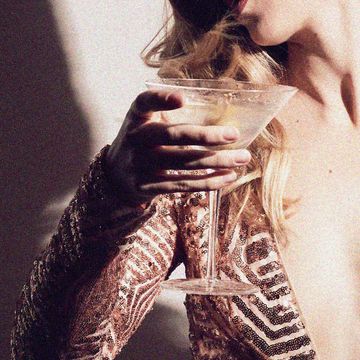 a woman in a gold sequin dress holding a cocktail with her face obscured
