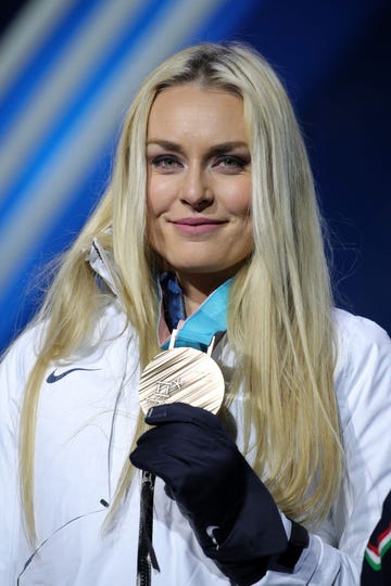 lindsey vonn smiles at the camera, she wears a white winter jacket and holds a medal hanging around her neck