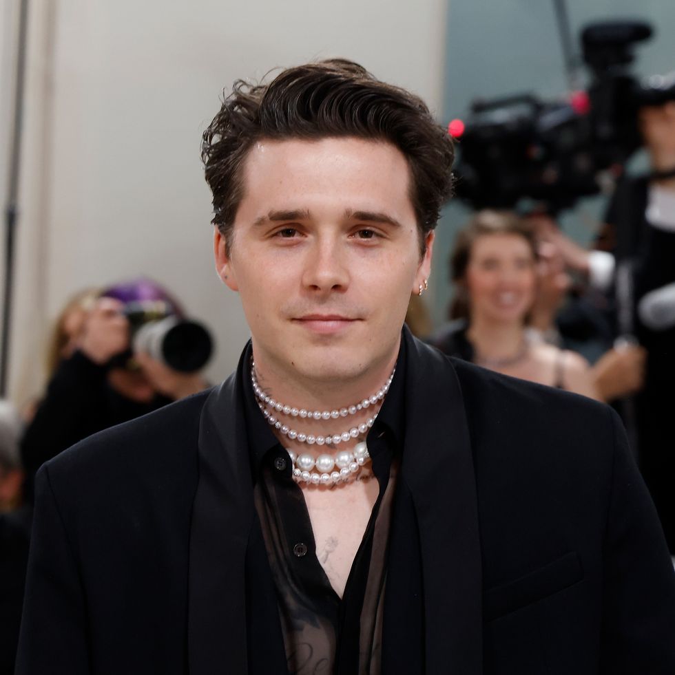 brooklyn beckham wearing a black suit with pearls around his neck at a fashion event