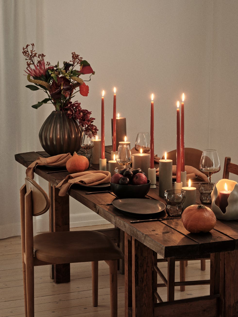 A wooden dining table is set for a meal, decorated with flickering candles and floral arrangements