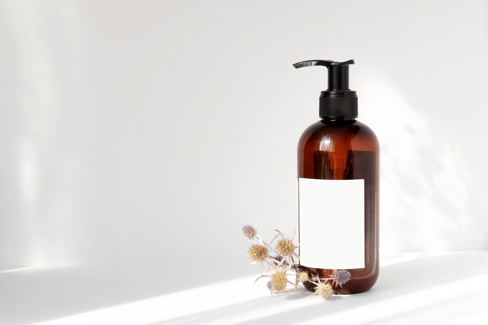 brown bottle with dispenser, empty label and bouquet of dried flowers next to it on white background in rays of light, with falling shadow concept of natural cosmetics