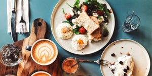 Brunch for two people with avocado toast, fried egg, salad, cappuccino and carrot cake served on the table, high angle view