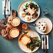 Brunch for two people with avocado toast, fried egg, salad, cappuccino and carrot cake served on the table, high angle view