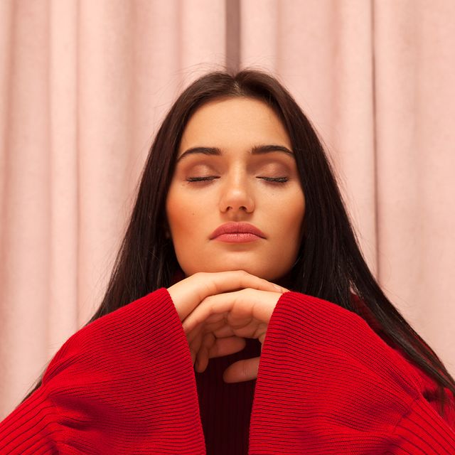 brunette woman wearing a red sweater closing her eyes