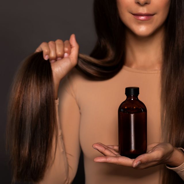 brunette girl with long straight and shiny hair　
beauty skin woman holding her strong and healthy hair and oil or shampoo bottle over grey background cosmetic hair beauty salon concept