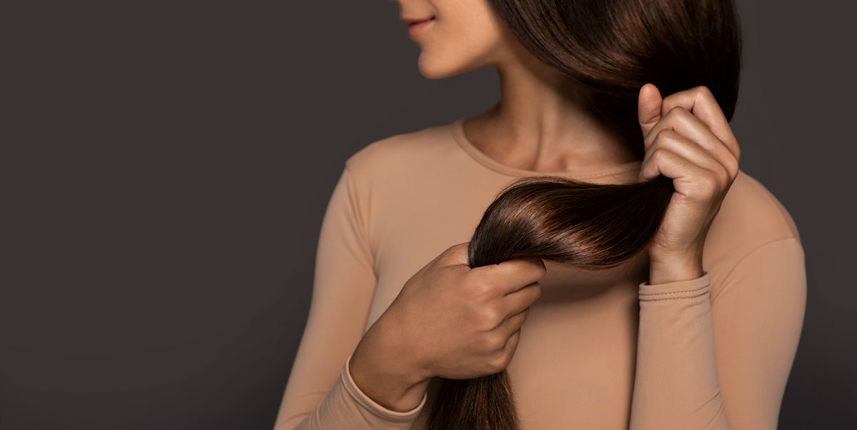 brunette girl with long straight and shiny hair beauty skin woman holding her strong and healthy hair in her hands over grey background cosmetic hair beauty salon concept