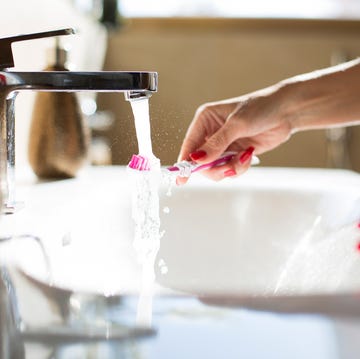 Woman rinsing her toothbrush, close-up of hands Brushing teeth at a bathroom sink with running water