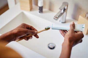 woman holding toothbrush and toothpaste by sink