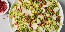 shaved brussels sprouts with pomegranates, shaved parmesan, and chopped toasted almonds in a white bowl