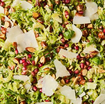 shaved brussels sprouts with pomegranates, shaved parmesan, and chopped toasted almonds in a white bowl