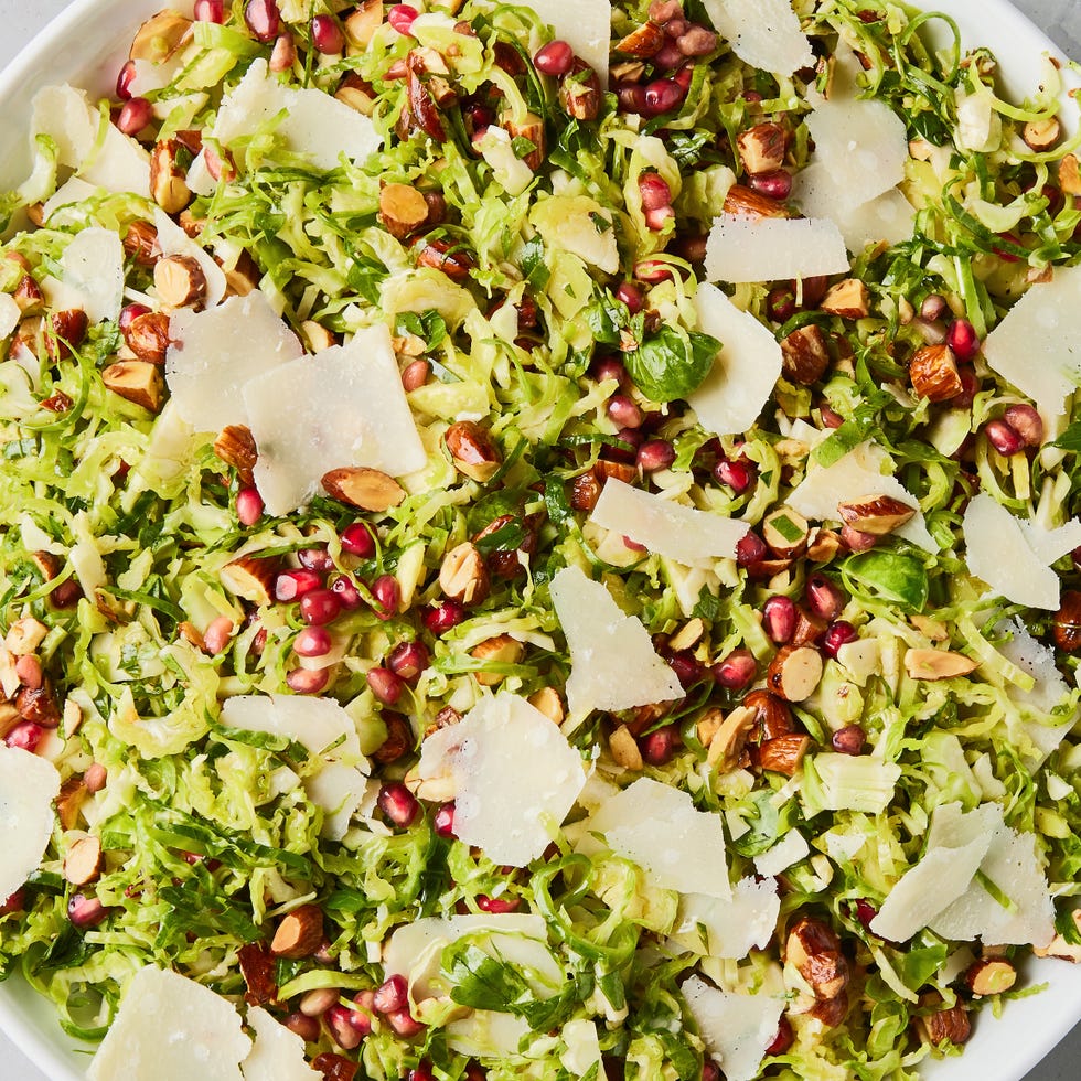 shaved brussels sprouts with pomegranates, shaved parmesan, and chopped toasted almonds in a white bowl