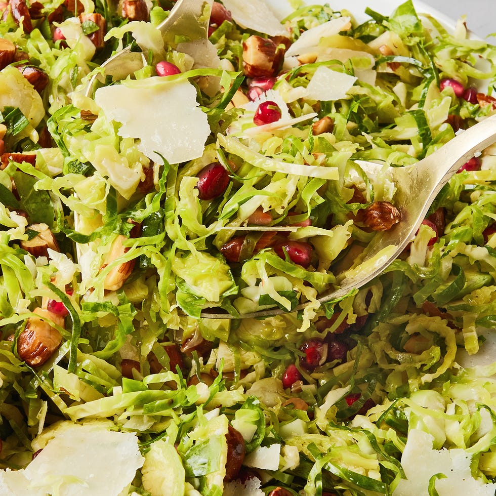 shaved brussels sprouts with pomegranates, shaved parmesan, and chopped toasted almonds in a white bowl