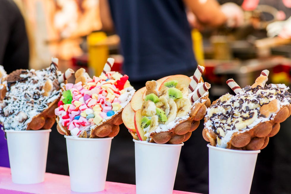 bubble waffles with raspberries, chocolate and marshmallow in white paper cups are sold on open kitchen food festival event street food in food stall