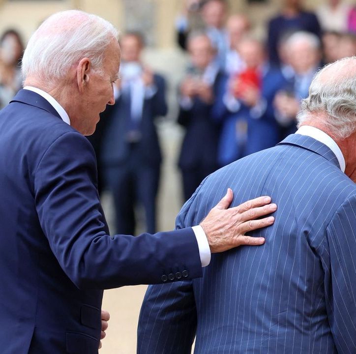 us president joe biden places his hand on the back of britains king charles iii as they walk in the quadrangle after ceremonial welcome at windsor castle in windsor, both wearing dark blu suits, with people clapping in the background