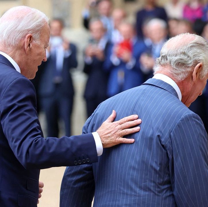 us president joe biden places his hand on the back of britains king charles iii as they walk in the quadrangle after ceremonial welcome at windsor castle in windsor, both wearing dark blu suits, with people clapping in the background
