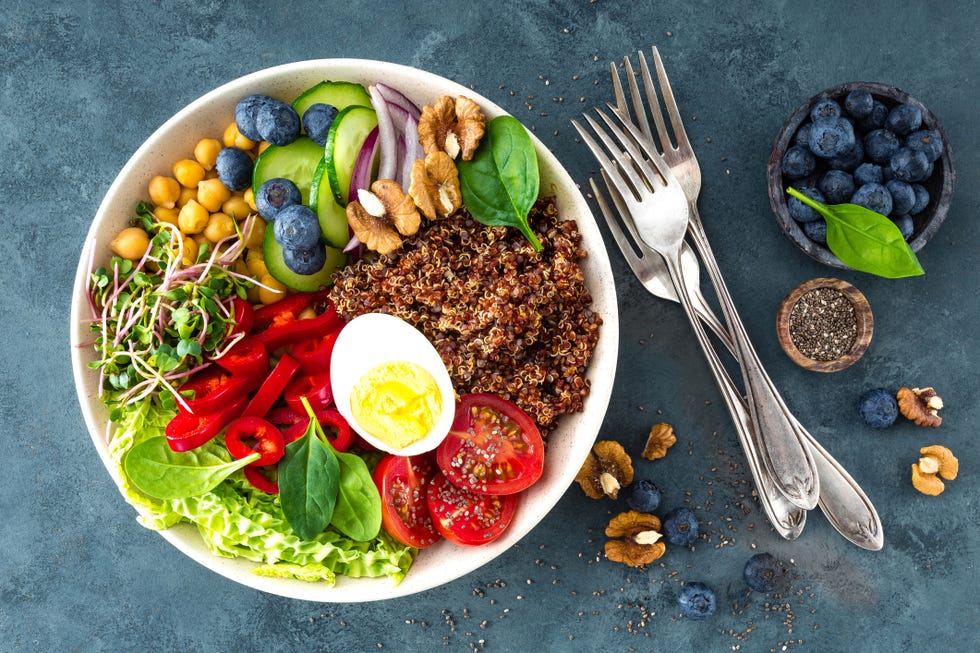 Buddha bowl dinner with boiled egg, chickpea, fresh tomato, sweet pepper, cucumber, savoy cabbage, red onion, green sprouts, spinach leaves, blueberry, walnuts, chia and quinoa. Healthy dish, lunch bowl. Detox diet. Balanced food. Top view