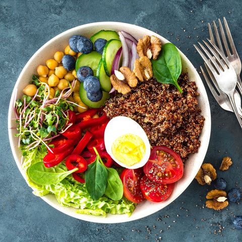 Buddha bowl dinner with boiled egg, chickpea, fresh tomato, sweet pepper, cucumber, savoy cabbage, red onion, green sprouts, spinach leaves, blueberry, walnuts, chia and quinoa. Healthy dish, lunch bowl. Detox diet. Balanced food. Top view