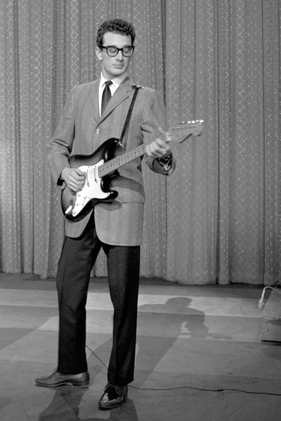 buddy holly plays electric guitar while standing in front of a diamond patterned curtain