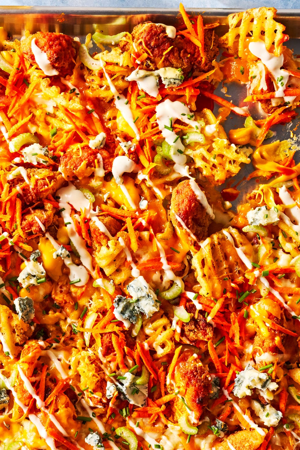 Buffalo Chicken Waffle Fry Nachos waffle fries on a sheet pan topped with buffalo chicken, carrots, celery, and blue cheese