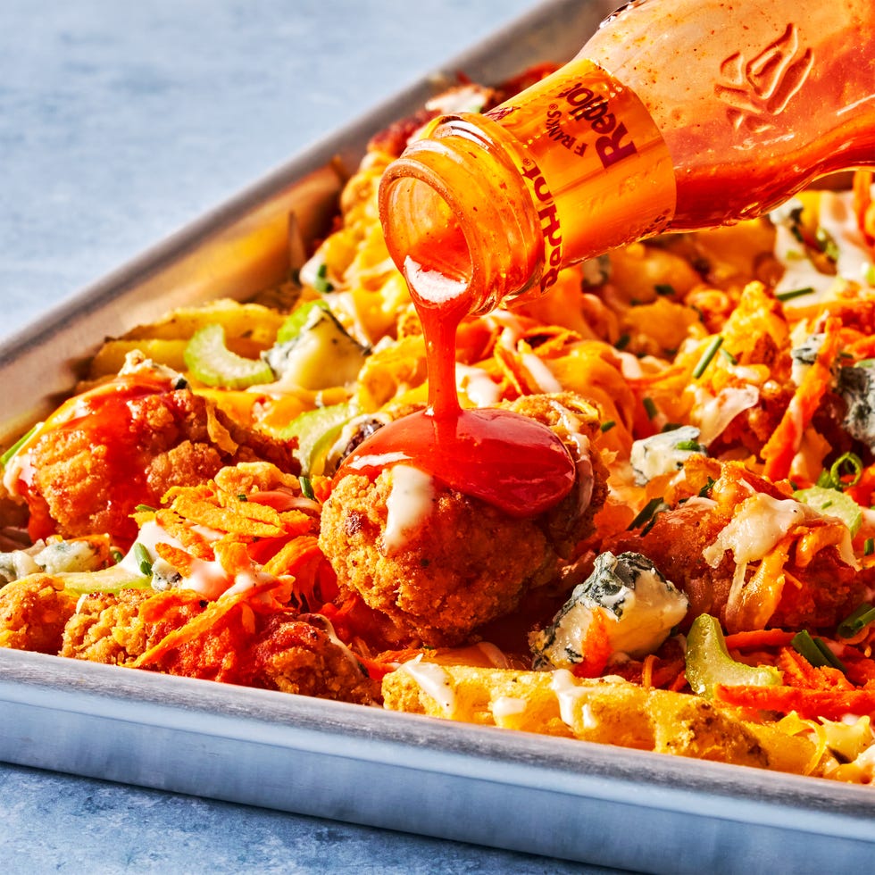 waffle fries on a sheet pan topped with buffalo chicken, carrots, celery, and blue cheese