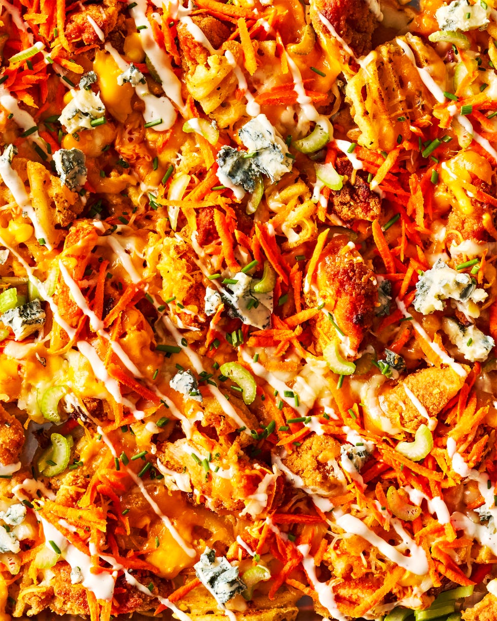 waffle fries on a sheet pan topped with buffalo chicken, carrots, celery, and blue cheese