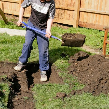 builder digging a trench in a garden with a spade