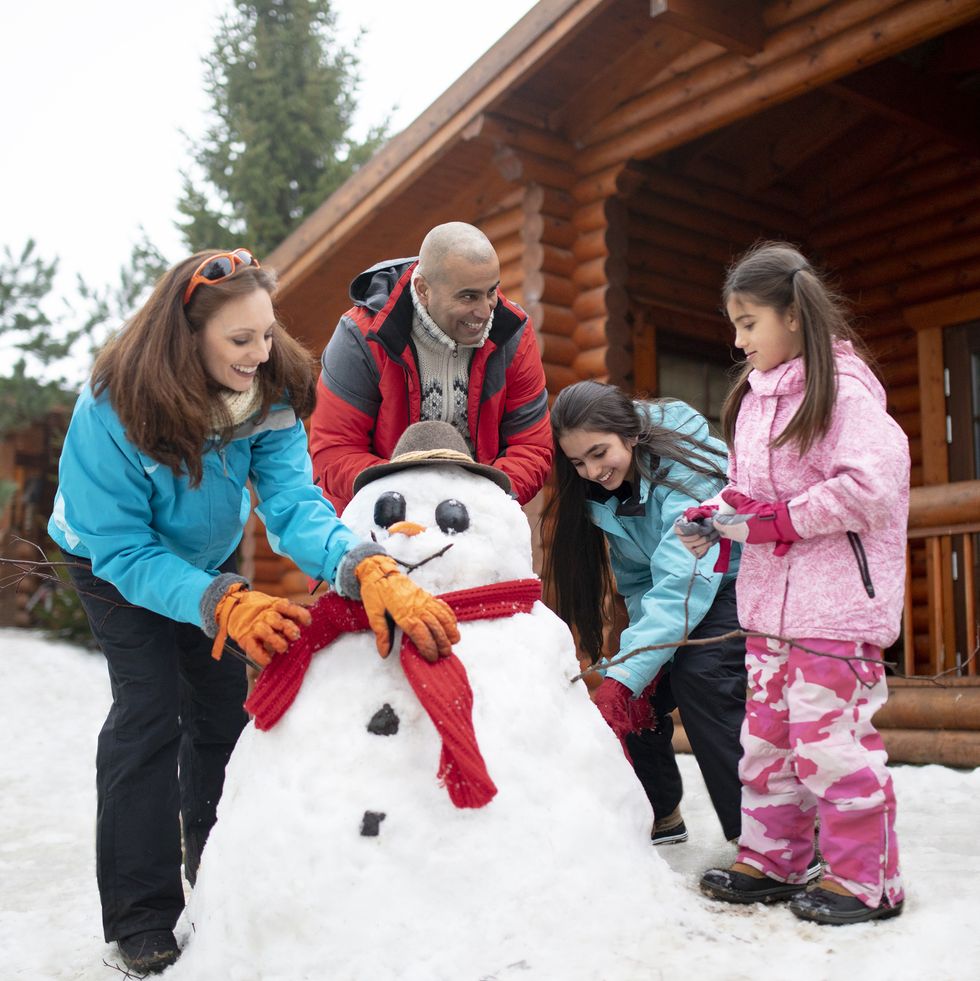 christmas activities  a multigenerational family building a snowman outside a log cabin