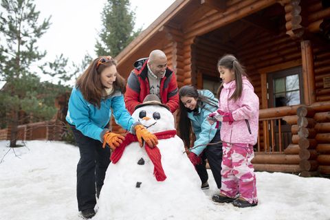 christmas activities  a multigenerational family building a snowman outside a log cabin