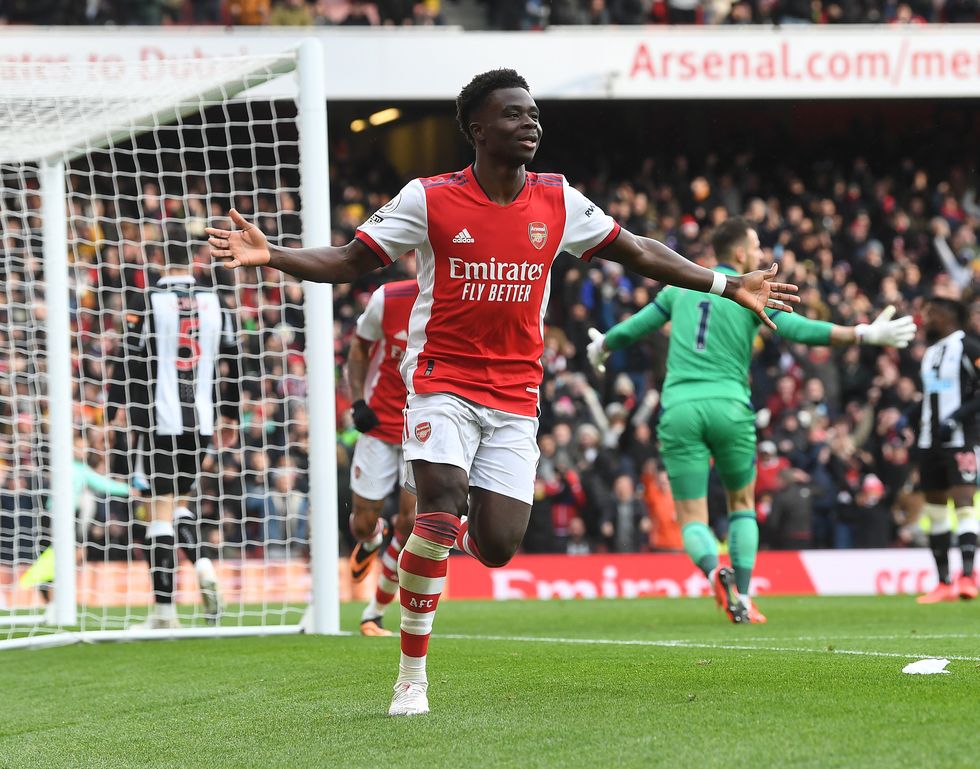 bukayo saka celebrates a goal in one of arsenal's premier league games, he is jogging along the side of the pitch away from the goal with his arms outstretched and smiling with joy