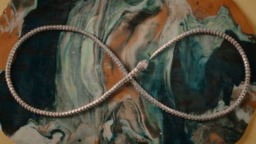 a silver necklace arranged in an infinity shape on a marbled surface
