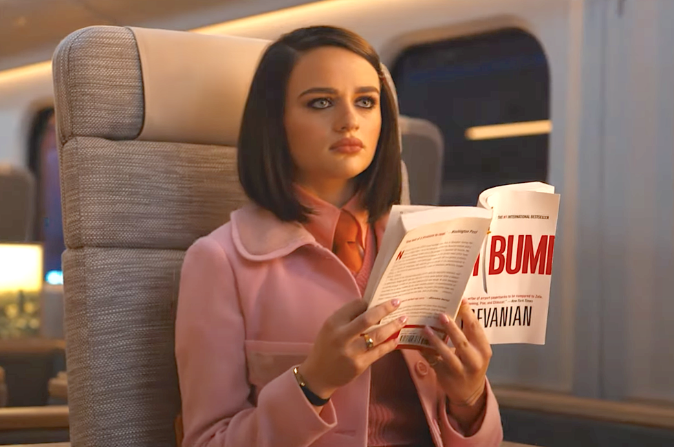 joey king sitting on a luxury bullet train, reading a book and wearing a pink jacket