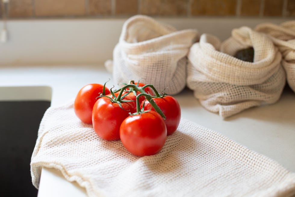 bunch of tomatoes on vine with reusable produce bags