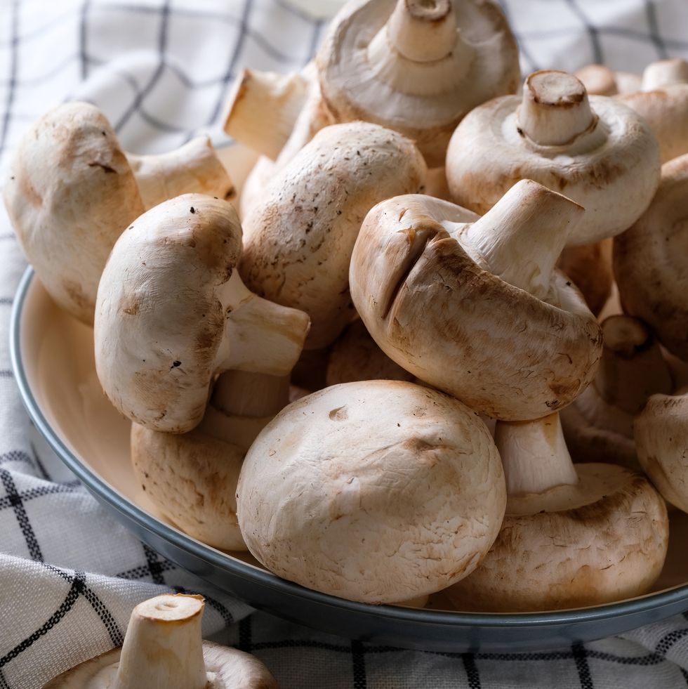 a bunch of whole raw fresh mushrooms in a plate, on a white table or background mushrooms are like vegetable protein the concept of vegetarian and vegan food and diet veganism and vegetarianism cooking at home or in a restaurant