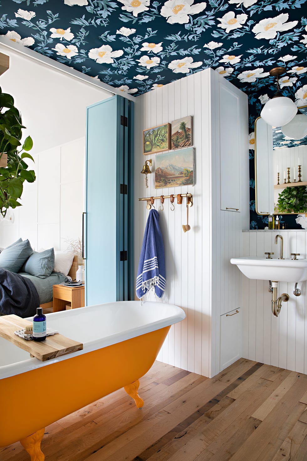 baño de estilo retro con bañera con patas amarilla, papel pintado floral en el techo y puertas plegables azules