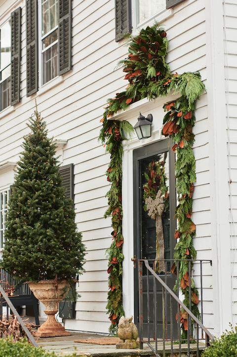 a front porch and door adorned with evergreen christmas decorations and lights