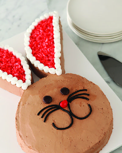 chocolate cake shaped like a bunny head with ears and a candy face